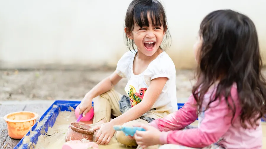 Two young girls playing in the sandbox, laughing and enjoying their time outdoors.