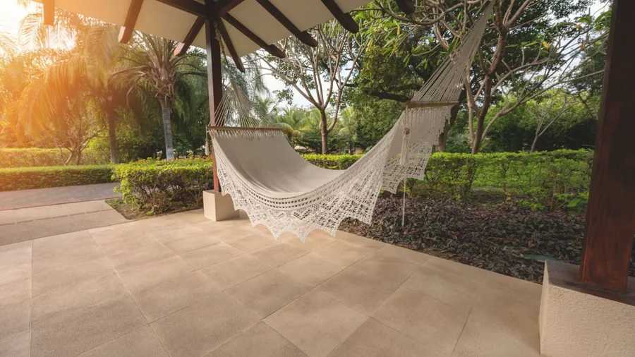 A hammock hanging under the shade on a patio.