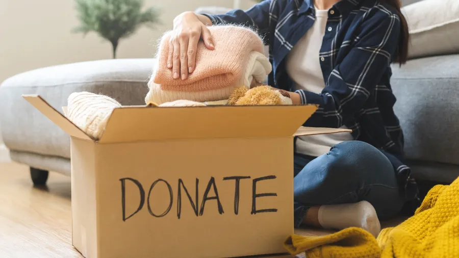 A woman putting folded clothes in a donation box.