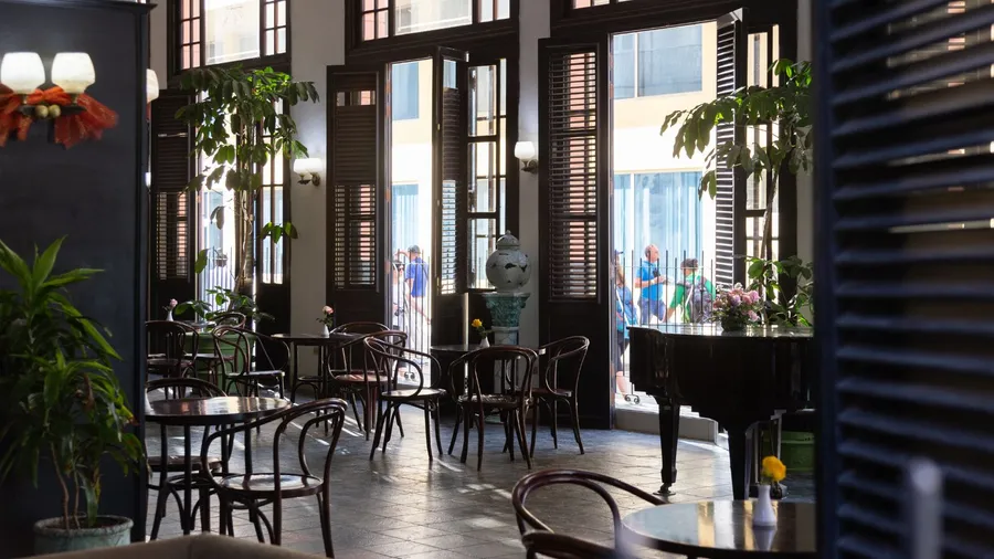 A cozy interior with dark wooden furniture and large windows, showing people outside.