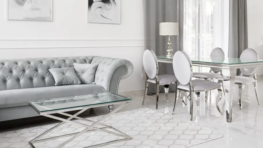 A white living room with a tufted sofa, glass coffee table, and light-colored curtains.