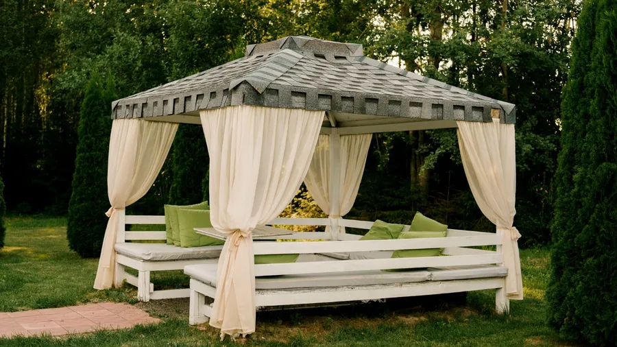 An outdoor gazebo with draped curtains and cushions, set in a garden.