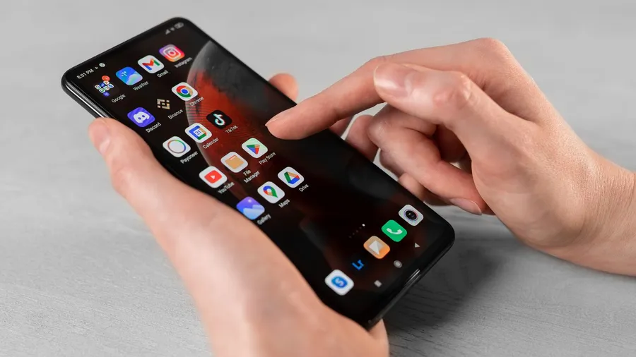 A person using a smartphone with home screen displaying many apps like Tiktok, YouTube, and Instagram.