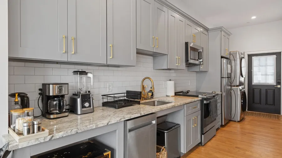 Modern kitchen with grey cabinets, marble countertops, and gold accents.