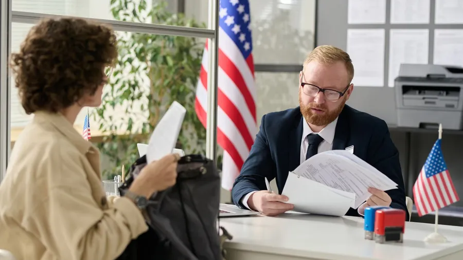 _2234701525 Portrait of male worker revising documents of young woman applying for visa in US immigration office