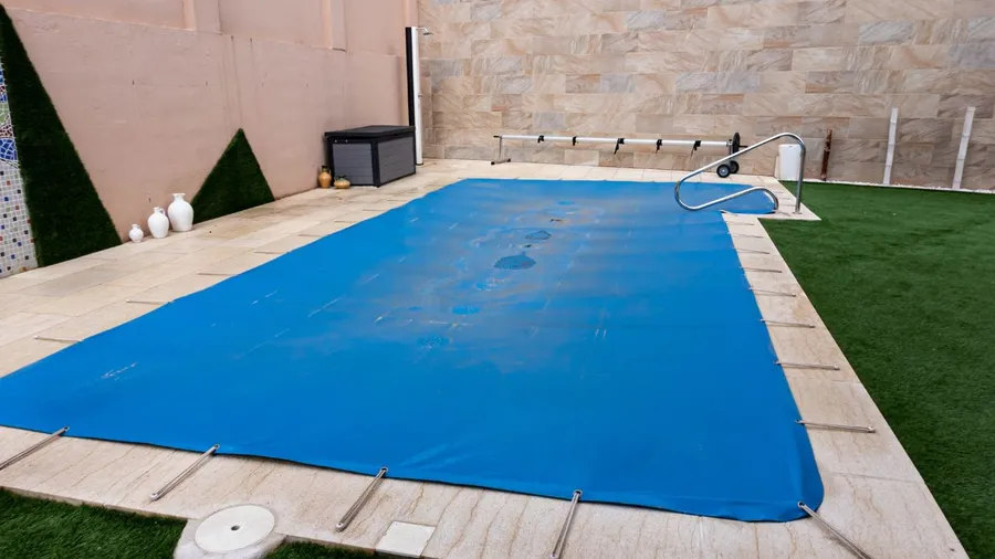 Pool cover laid out on an outdoor swimming pool with tiled deck.