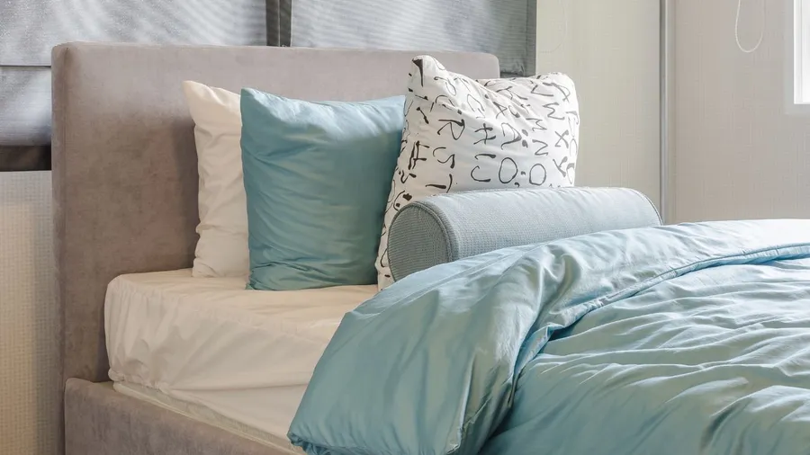 A bedroom with a bed that has white and light blue sheets, pillows, and a headboard.