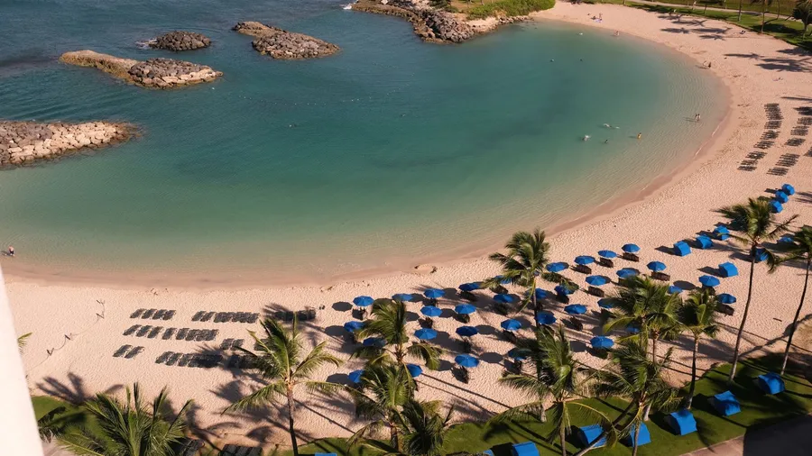 Oahu, Hawaii lagoon, beach and Pacific Ocean showing the straw umbrellas, blue beach chairs on the sand of the beautiful lagoon.