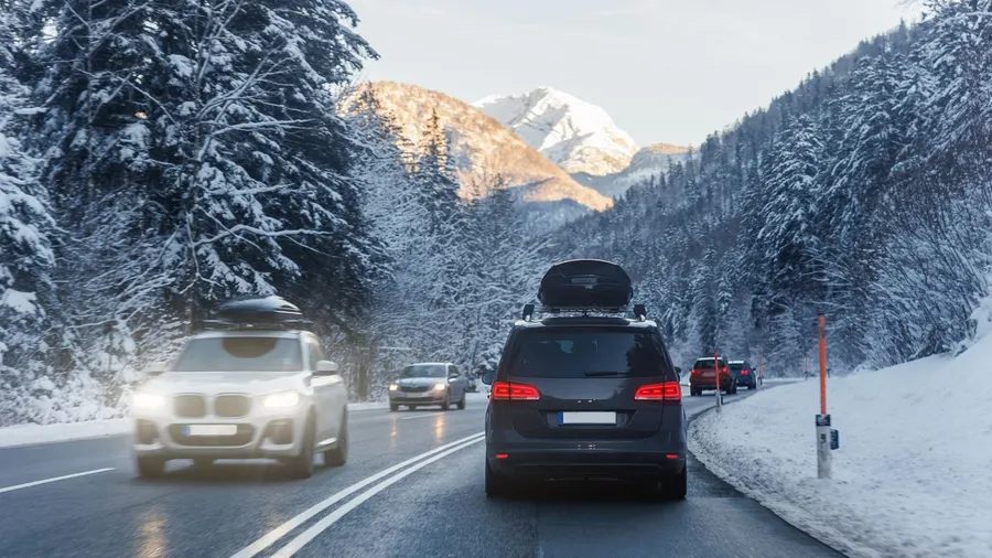 Scenic rear view of a family van with a roof box and luggage driving along an alpine countryside road on a cold winter day near a European mountain resort.