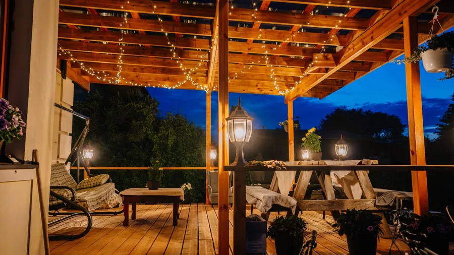 A patio with wooden furniture, lanterns, plants, and string lights draped over a pergola.