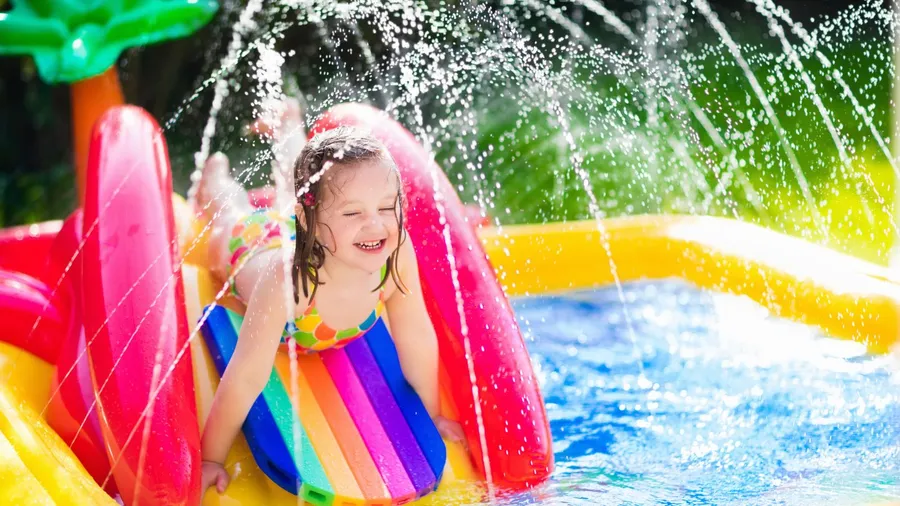 Child smiling and splashing in a colorful backyard water slide.
