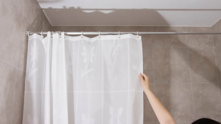 A person opening a white floral shower curtain.