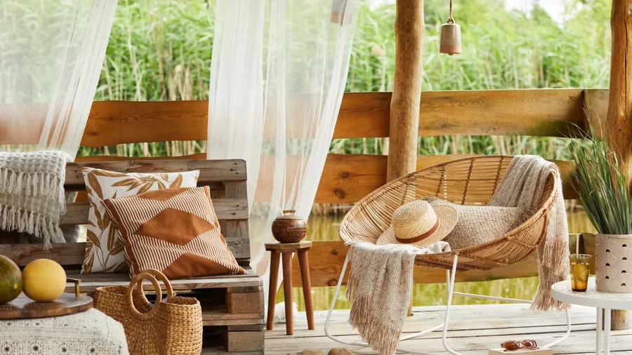 A cozy outdoor lounge area with a wooden pallet bench and wicker chair overlooking a pond.