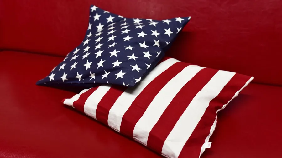 Two decorative pillows with American flag designs, resting on a red couch.