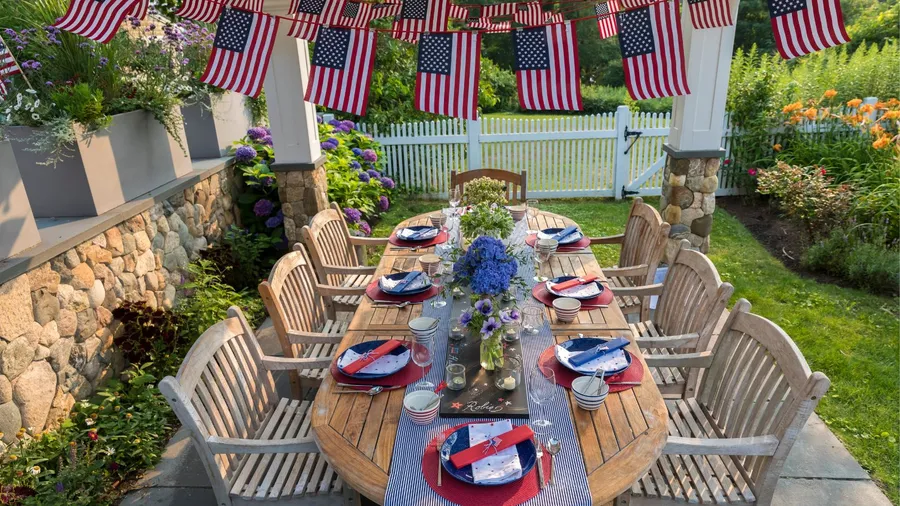 Festive table setting for memorial day with blue striped table runner, red chargers, blue plates, and flag bunting hanging above the table.