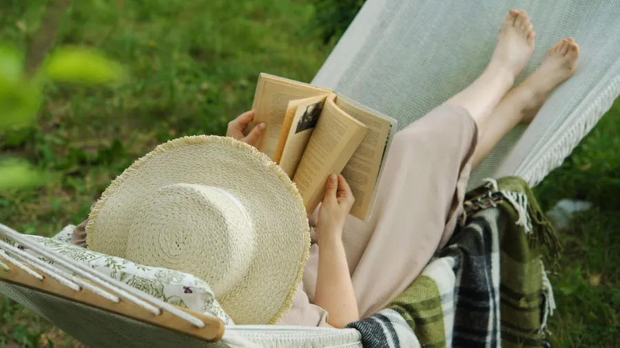 A woman reading a book on a hammock.