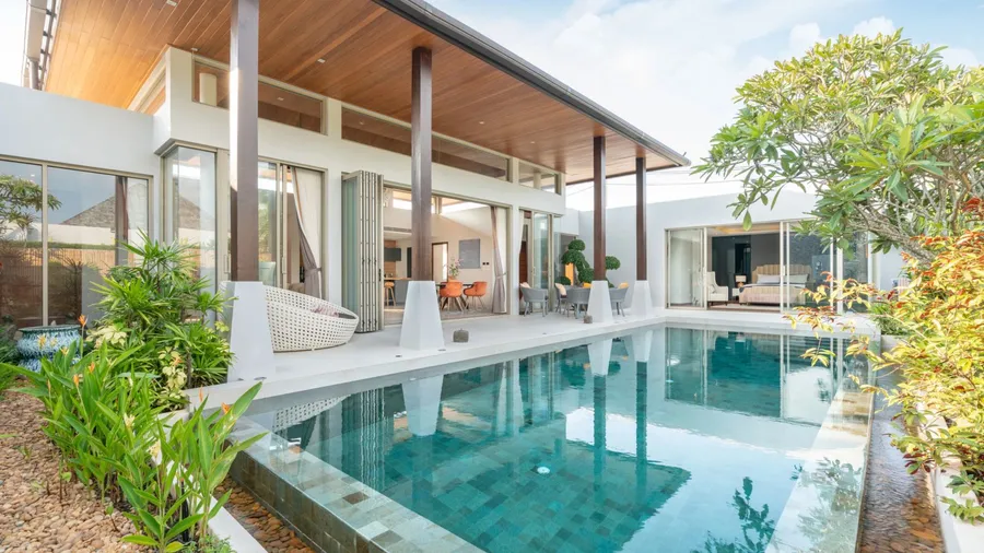 A modern home with a pool and patio, surrounded by greenery and bright sunlight.