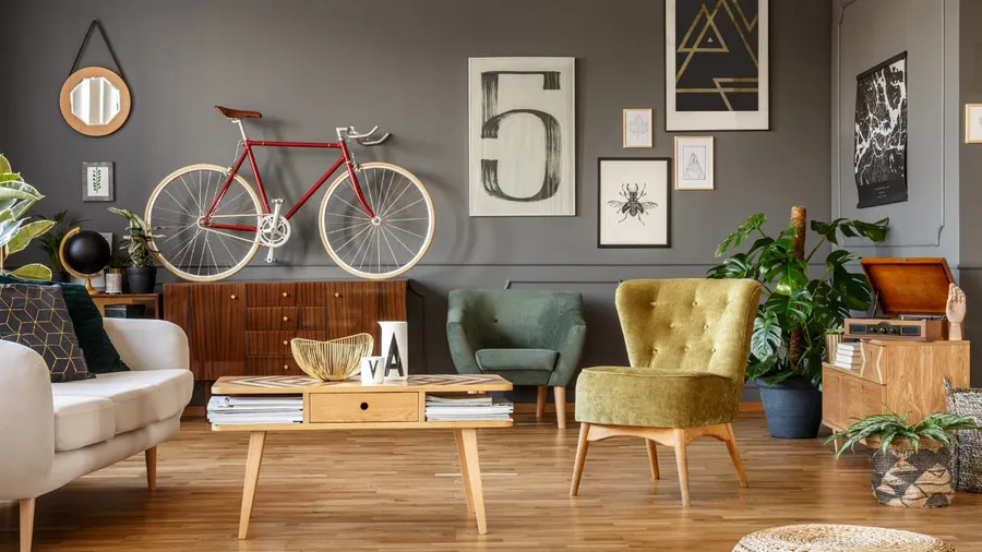 A living room interior with art collection on a gray wall, wooden coffee table, armchair, plant, and a red bike.