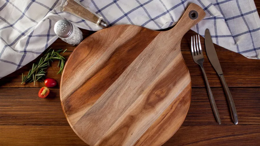 A wooden cutting board with a fork, knife, and a sprinkle of herbs beside fresh tomatoes.