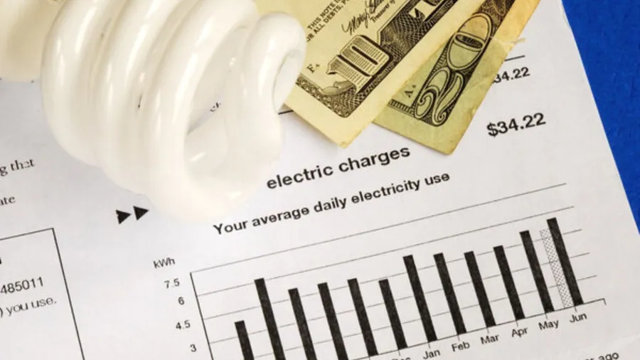 The image features a compact fluorescent light bulb and few dollar bills placed on top of an electricity bill.