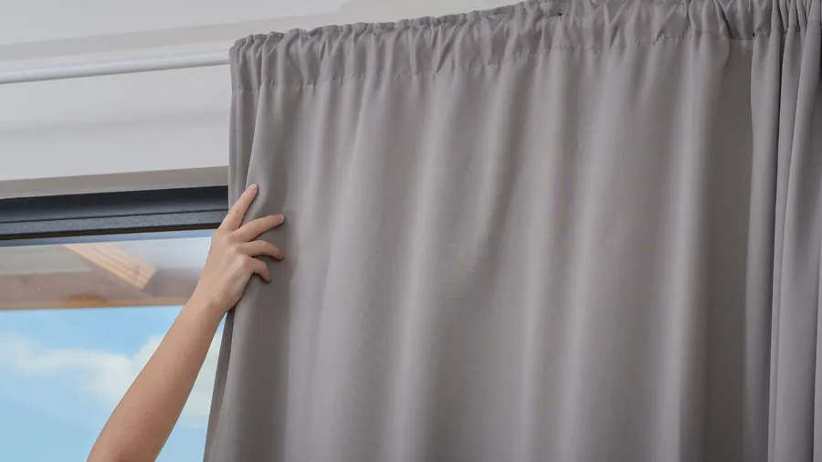 A woman covering the window with gray blackout curtains.