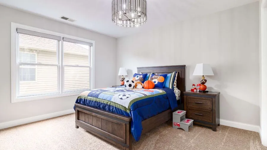 A bedroom interior with sports themed bedding, rustic wood nightstand with lamp, and carpet.