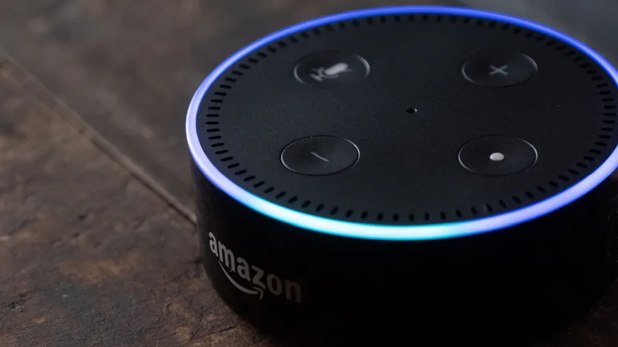 A voice activated amazon echo dot speaker on a wooden surface.