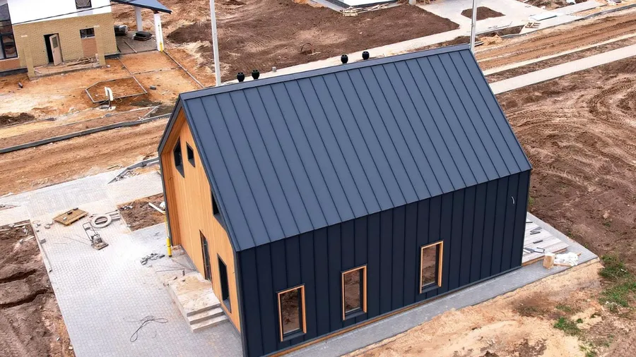 A small modern house with black metal siding and wooden accents on a construction site.