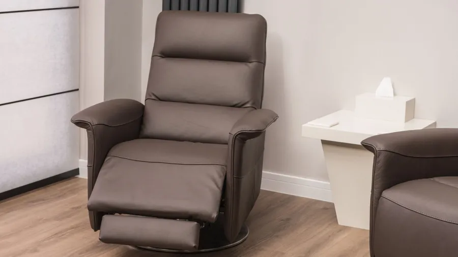 A brown leather recliner on a wooden floor and a white table in front of a white wall.