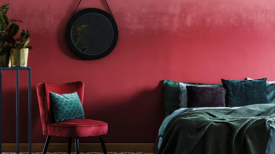 A bedroom interior with burgundy accent wall, cozy bed with green bedding, and a burgundy armchair.