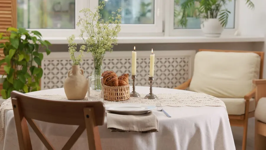 A bright breakfast nook with a table, vase with flowers, candles, and a cushioned seating area.