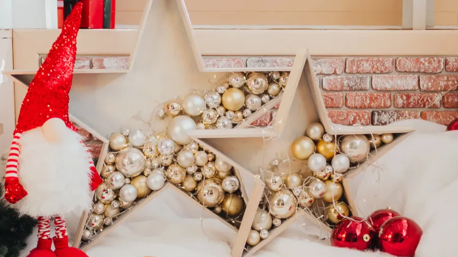 Colorful holiday decorations fill a warm space featuring two large stars filled with shiny ornaments. A festive gnome stands nearby, creating a joyful atmosphere for the season.