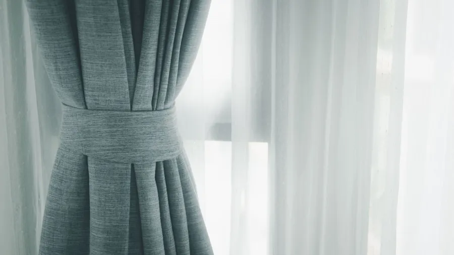 Layered curtains on a window with gray blackout curtains and white sheer curtains.