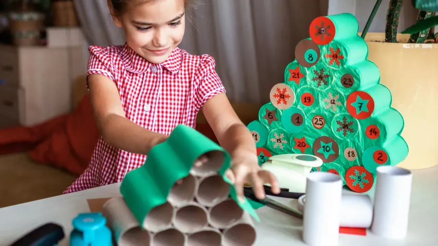Cute little kids making handmade advent calendar with toilet paper rolls at home. Glue, colored paper, cut punch to hide sweets and candies in rolls. Seasonal activity for kids, family winter holidays