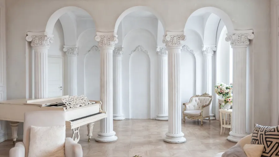 An elegant white space with classical columns, featuring a grand piano and luxurious seating arrangements.