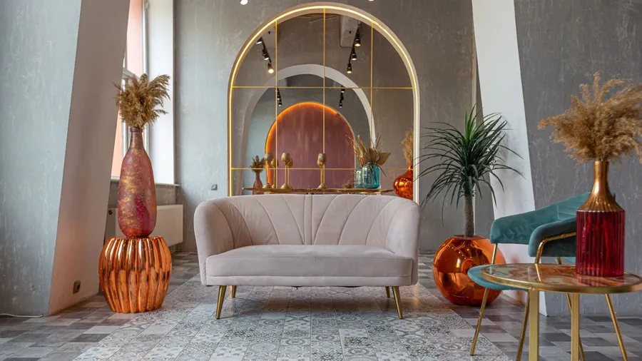 Elegant living room with a cream sofa, gold-accented vases, and reflective wall decor in warm tones.