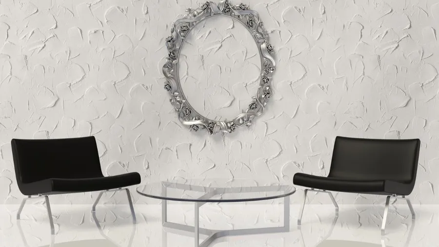Two black chairs with a glass table in the middle, against a textured white wall with a decorative mirror.