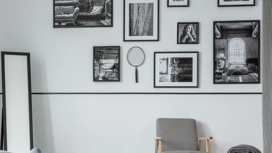 Gallery of black and white photos on wall of stylish bedroom interior with mirror, retro armchair and wooden table with blanket
