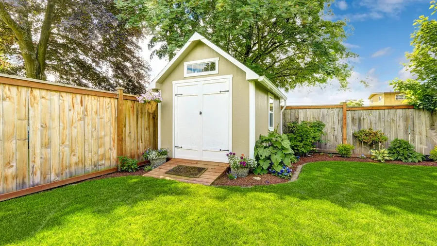 Green lawn with a small garden shed, bordered by plants and flowers.