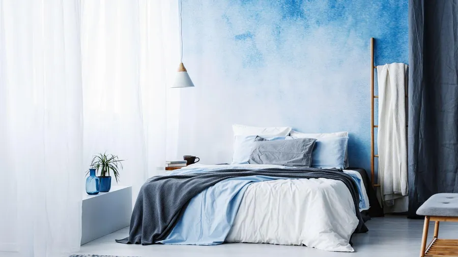 An aqua theme bedroom with cozy bed, blue throw, wooden ladder, small potted plant, and sheer curtains.
