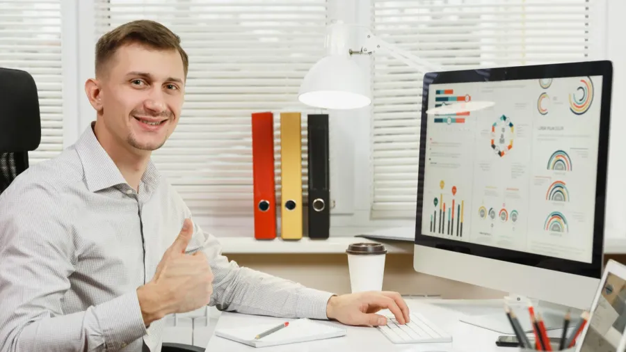 Handsome smiling business man in shirt sitting at the desk, show