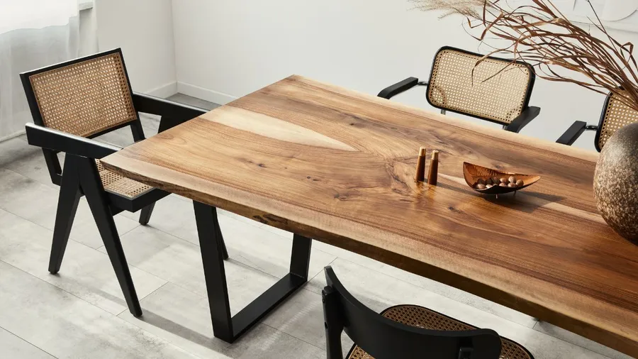 A modern dining room with a large wooden table, black and rattan chairs, and decorative vase.