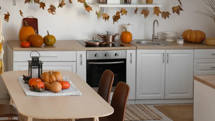 A kitchen interior decorated with pumpkins and dried leaves.