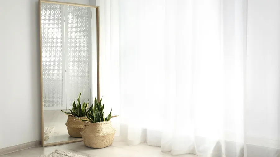 A large mirror with wooden frame and a potted plant placed near a window.