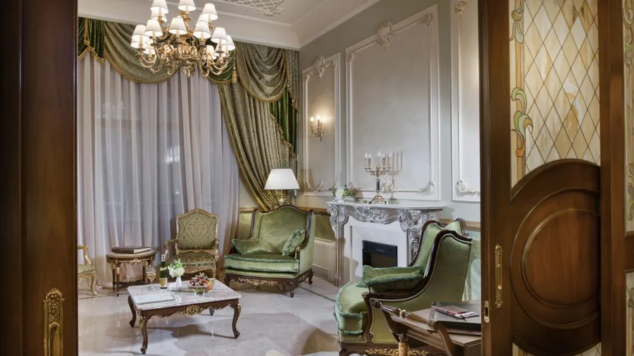 A luxurious living area features green upholstered furniture, a chandelier, and elegant decor against muted walls.