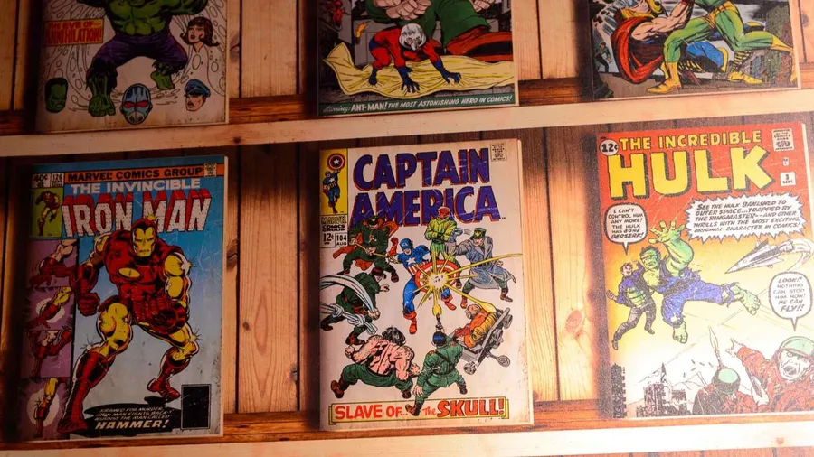 Front-facing superhero comics on a wooden shelf.