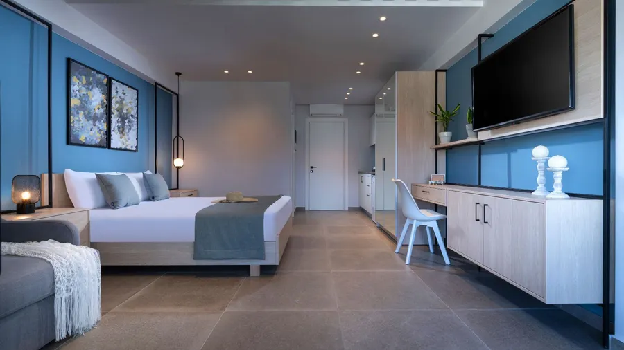 Modern studio apartment in blue theme featuring bed, wall-mounted tv screen, wall-mounted able and chair.