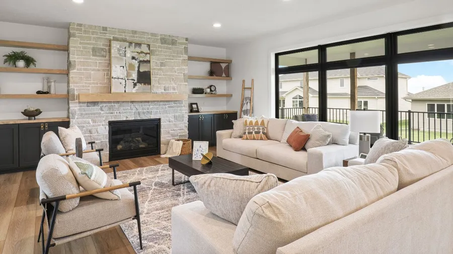 A modern living room features a stone fireplace, comfortable seating, and large windows allowing natural light.