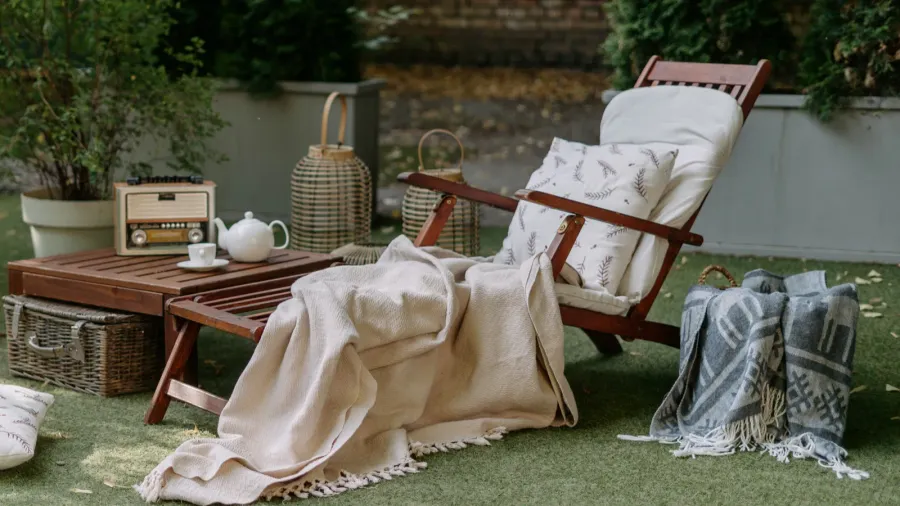 Outdoor garden wooden furniture at autumn nature, green grass. Nobody at home backyard with chair, lounge. Relax at outside terrace with blankets, pillows at retro, vintage decoration.
