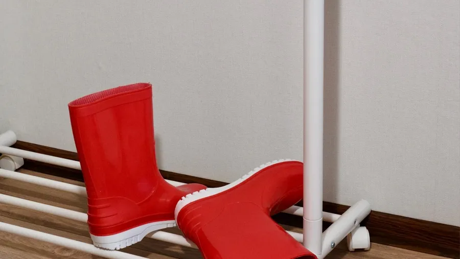 A pair of red rubber boots resting on a rack against a wall.
